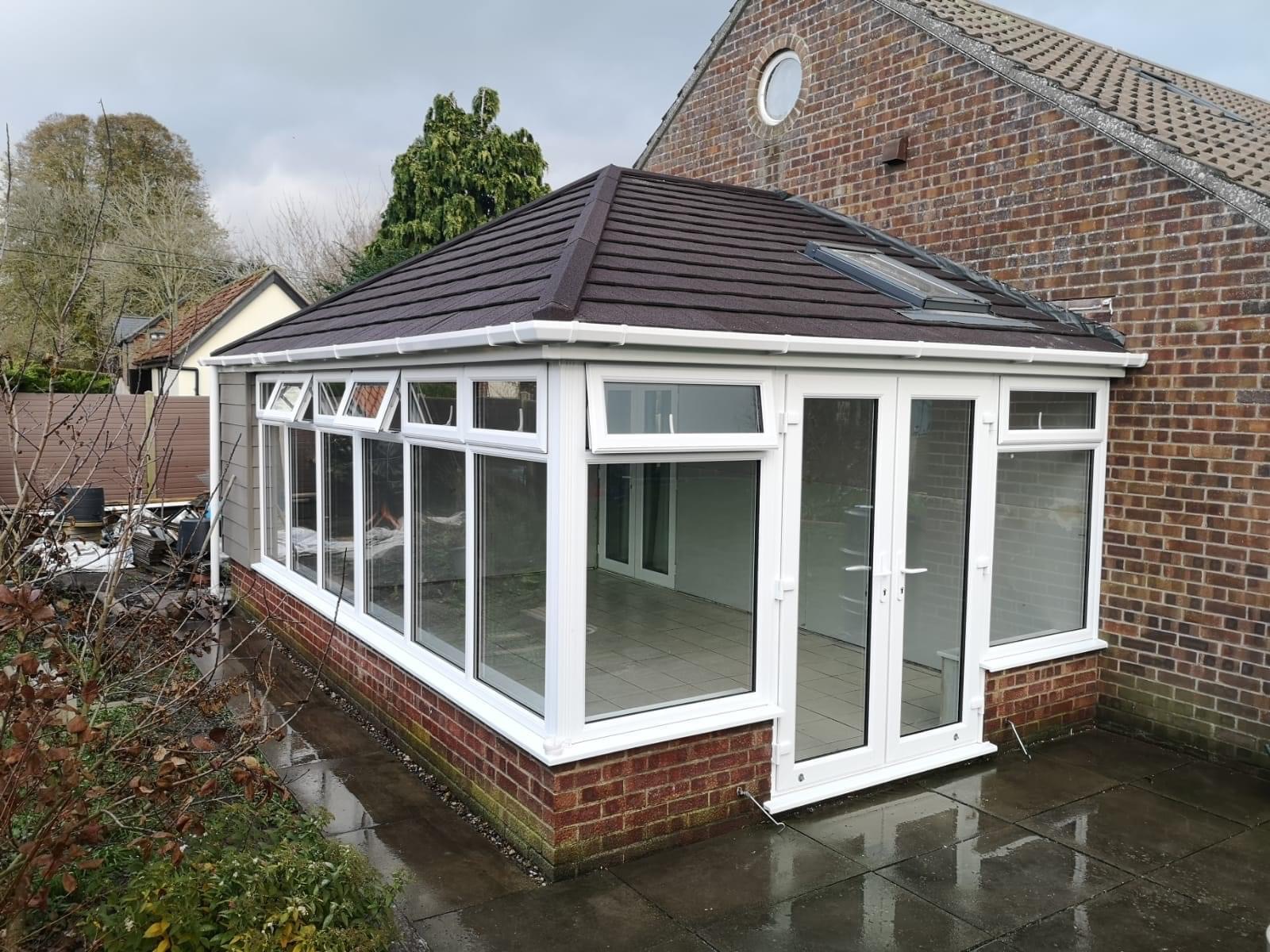 Tiled conservatory with white framed uPVC windows and door on a rainy day