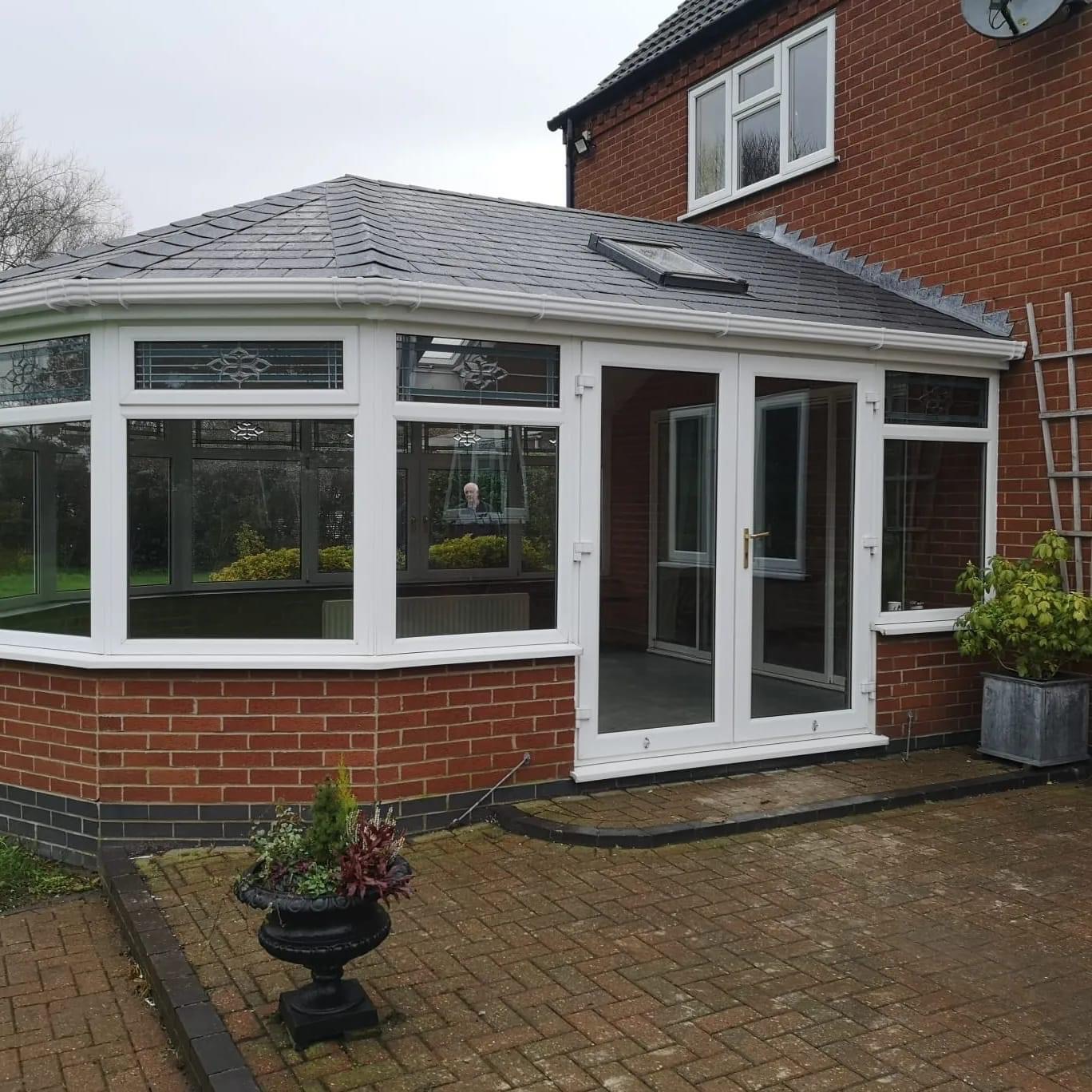 Outside view of tiled conservatory with wite frames and grey slate and next to potted plants